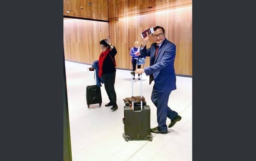 Sam Rainsy walks with his wife Tioulong Saumura while holding a suitcase and his passport, in this photograph posted to Sam Rainsy's Facebook page.
