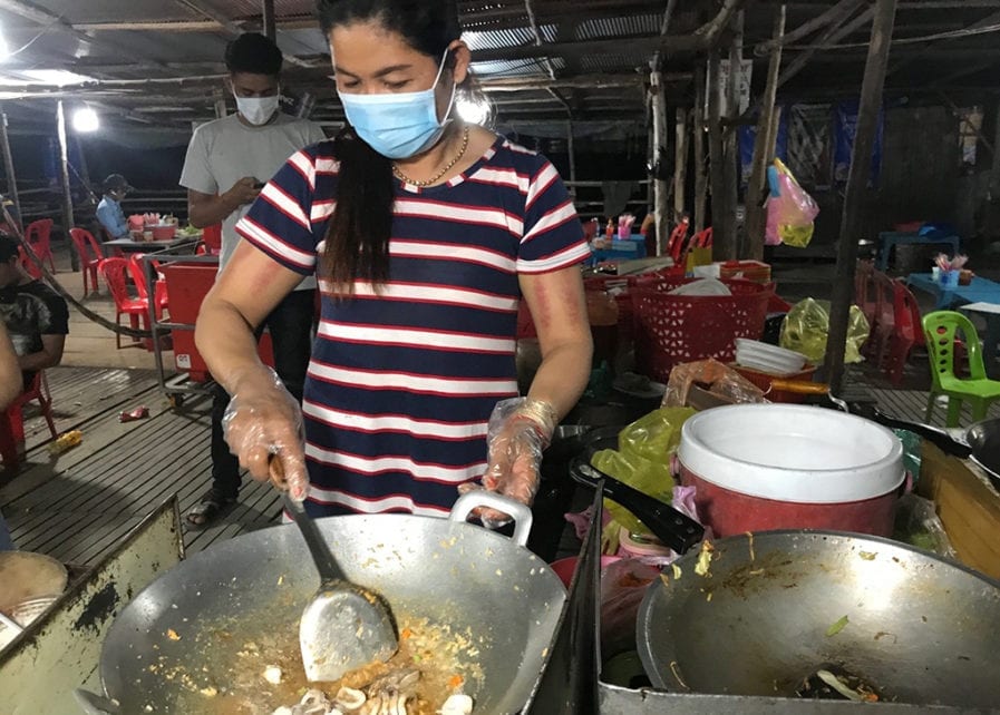 Chan Mach, 43, cooks while wearing a mask at her roadside restaurant in Takeo province in late March 2020. (Ouch Sony/VOD)