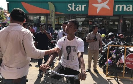 Khan Chanthorn, wearing a T-shirt depicting slain political analyst Kem Ley, is stopped and held by a security officer on July 8, 2020, after Chanthorn had rode his bicycle into the Caltex gas station to commemorate the four-year anniversary of Kem Ley's death at the site where he was killed. (Cambodian Youth Network)