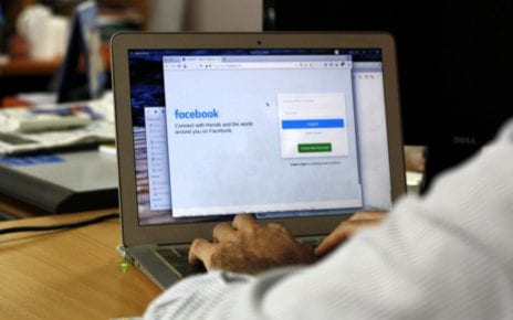 man types on laptop with screen showing Facebook login
