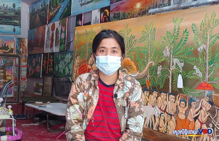 Kim Soth, an artist, wears a mask while sitting in front of her paintings in Siem Reap city's Nokor Thom commune on July 5, 2021. (Pork Kheuy/VOD)