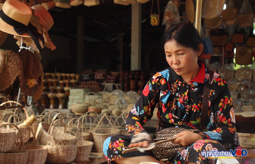 Handicraft vendor Khun Siwon polishes a wooden spoon inside her shop stocked with dozens of woven baskets in Siem Reap city's Nokor Thom commune on July 5, 2021. (Pork Kheuy/VOD)