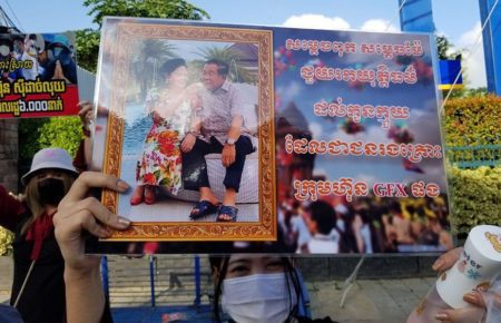 A masked protestor holds up a protest sign depicting Prime Minister Hun Sen and wife Bun Rany during a protest for compensation from the GoldFx scam at the premier's house, in a photo provided by an investor on August 16, 2021.
