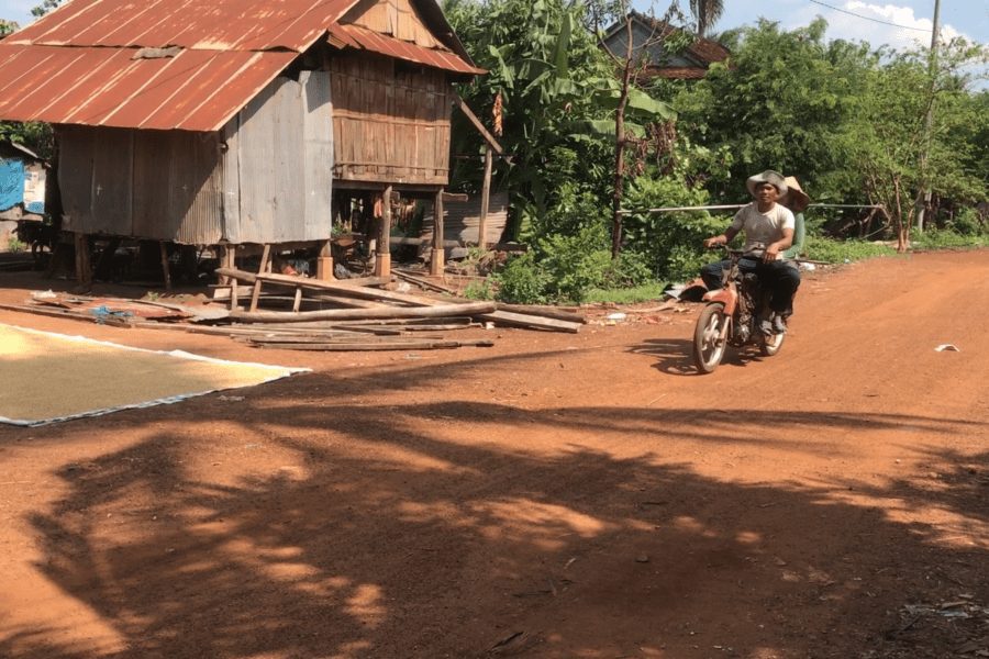 A man and woman drive a motorbike past a stilted house in Tbong Khmum province. (Chorn Chanren/VOD)