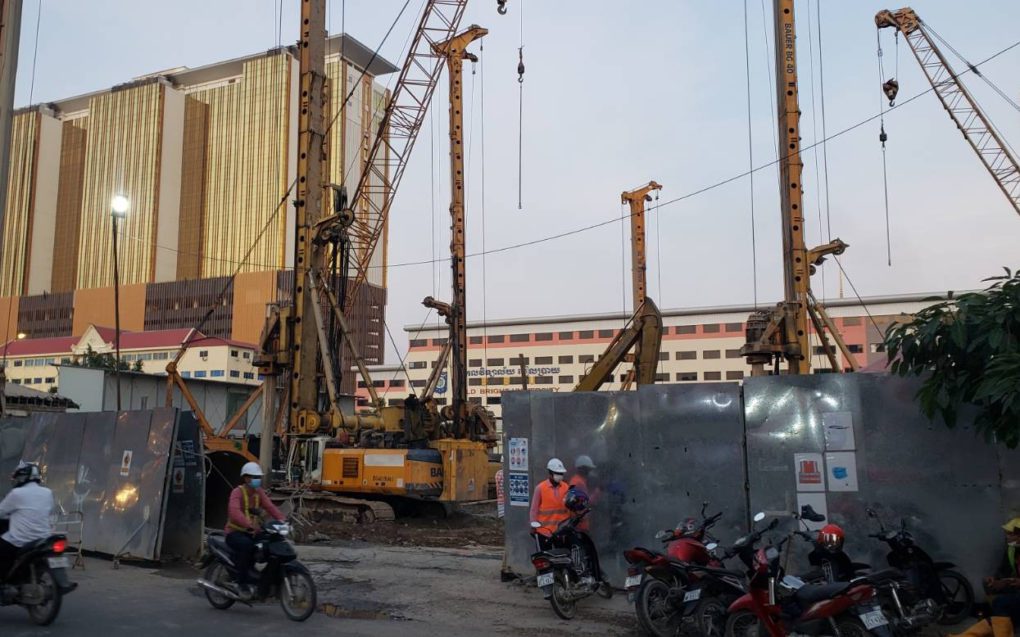 A worker rests on a motorbike in front of the Naga 3 construction site as another drives past on October 28, 2021. (Danielle Keeton-Olsen/VOD)