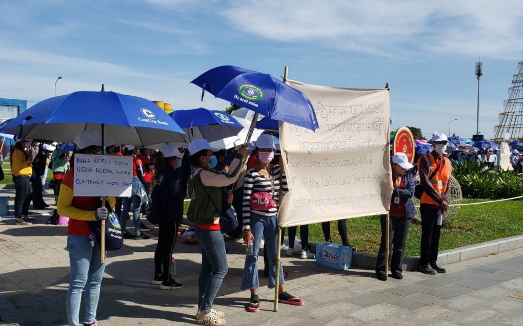 Workers hold umbrellas and protests signs, urging the company to "stop using illegal work contract" and "comply with article 279 of the labor law", at the park in front of Naga 1 on December 18, 2021. (Danielle Keeton-Olsen/VOD)