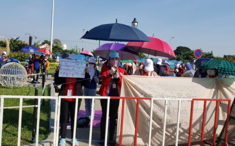 A worker stands behind the barricade with an umbrella and sign asking for NagaWorld to reinstate 365 terminated workers during the fourth day of a strike against NagaWorld's alleged labor rights violations on December 21, 2021. (Danielle Keeton-Olsen/VOD)