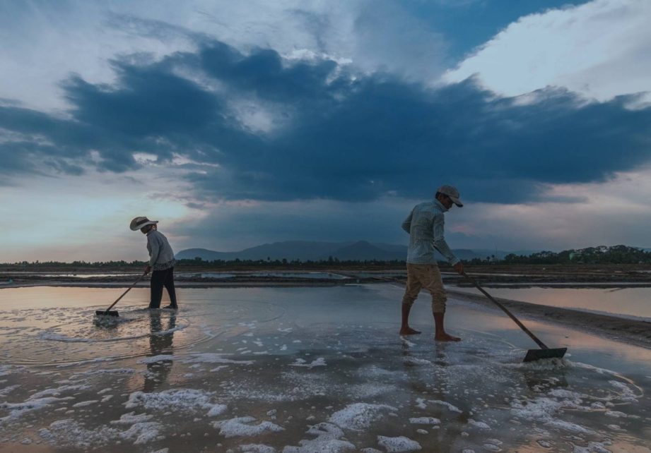 Two salt producers push water across a salt flat in Kampot province in June 2021. (You Bunchan/VOD)