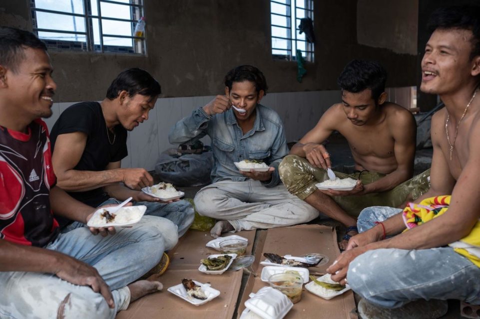 Construction workers Sun Kim Yan, Sim Ry, Dieb Phearum, Phan Sochantra and Sim Rib eat lunch on a construction site in Kambol District, Phnom Penh. All come from the provinces, all except Phearum have debts to microfinance institutions and all of them have experienced not being paid on time whilst working in the construction industry. (Andy Ball)