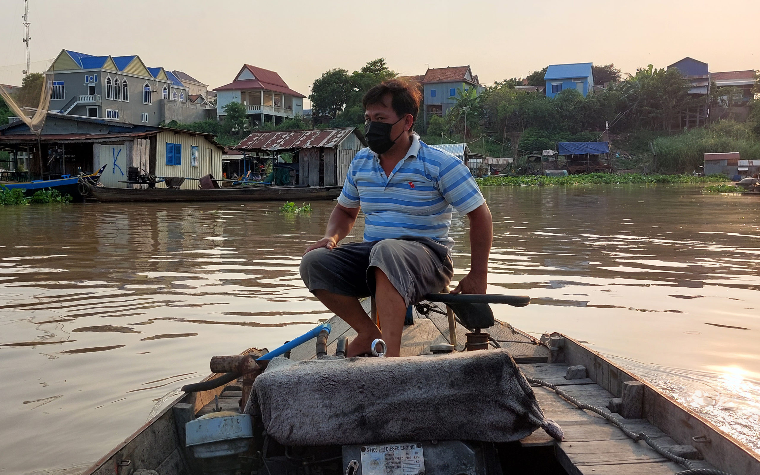 Yor Yeng Tam, 45, steers his motorized boat between floating houses and dai on the Tonle Sap river in Phnom Penh's Prek Pnov district on March 15, 2022. (Danielle Keeton-Olsen/VOD)