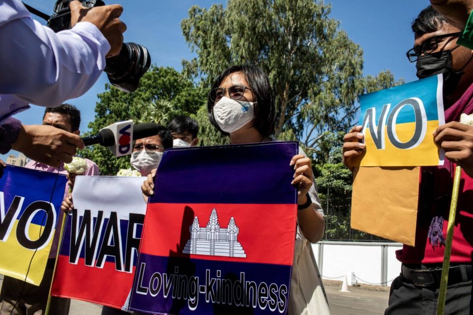 Phuon Keoreaksmey holds a Cambodian flag poster with the words "Loving-Kindness" on it in front of the Russian Embassy as a photographer takes a photo on April 5, 2022. (Roun Ry/VOD)