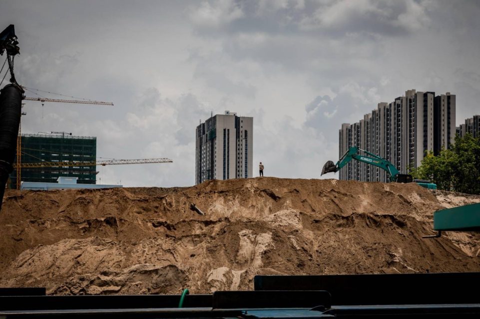 A man stands on top of a pile of sand as an excavator digs nearby at a sand depot in Phnom Penh on May 11, 2022. (Roun Ry/VOD)