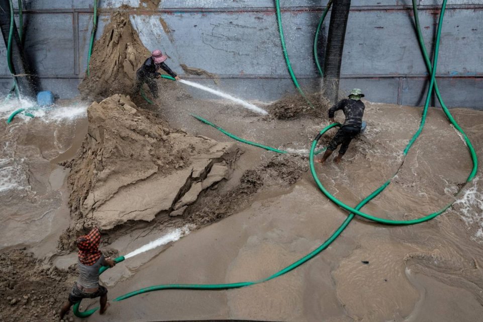 Sand dredging workers use the pressure of water from a hose to push sand into a pipe that will transport it to a sand depot or construction site, in a sand barge in Phnom Penh on May 11, 2022. (Roun Ry/VOD)