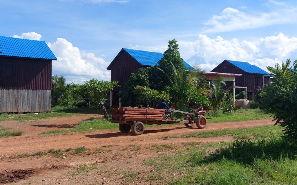 A man drives a "koh yun" tractor stacked with timber past three houses in the Srekor Thmey village resettlement houses in Stung Treng province on May 20, 2022. (Danielle Keeton-Olsen/VOD)