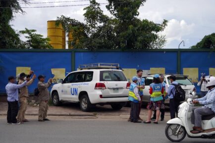 UN observers in blue vests stand in front of their parked car, with plainclothes people taking photos of them, during the NagaWorld strike in Phnom Penh's Tonle Bassac district on August 17, 2022. (Hean Rangsey/VOD)