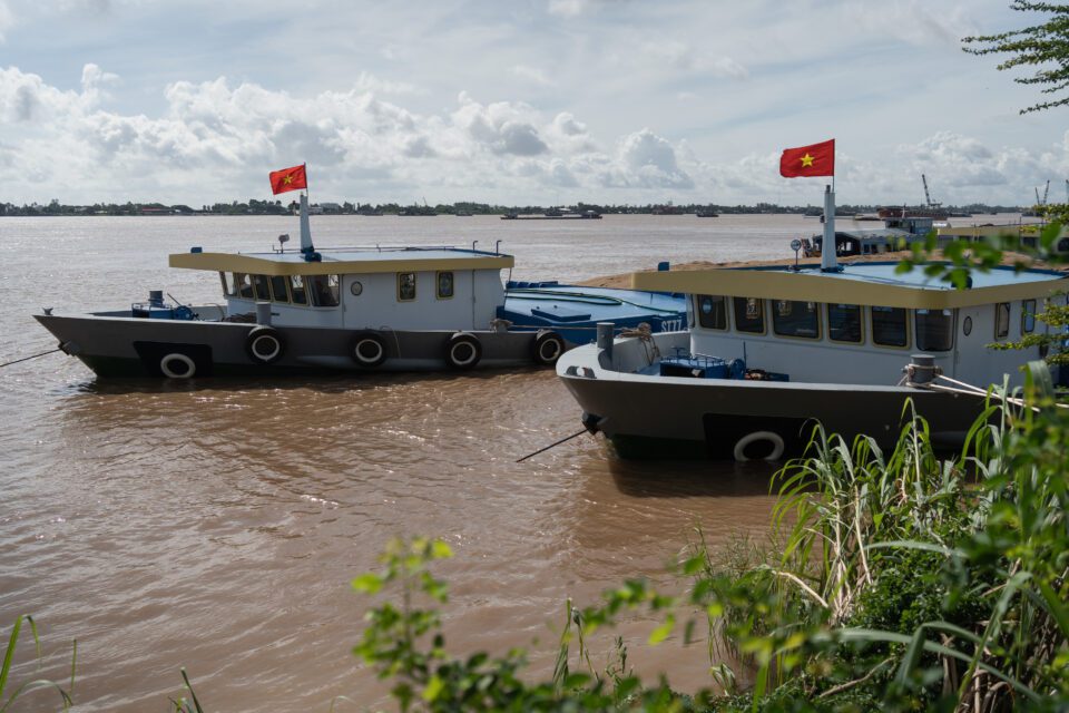 Sand mining barges flying the Vietnam flag and full of sand moored on the side of the Mekong. (Andy Ball)
