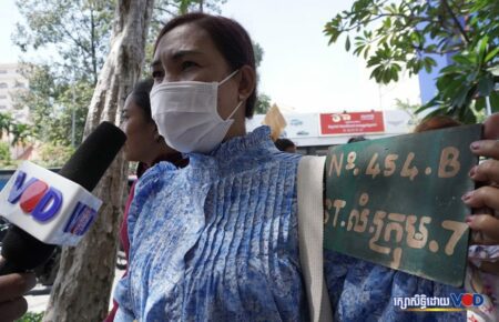 A woman protesting the road expansion in Phnom Penh's Russei Keo district holds an address marker while speaking to a reporter on November 1, 2022. (Hean Rangsy/VOD)