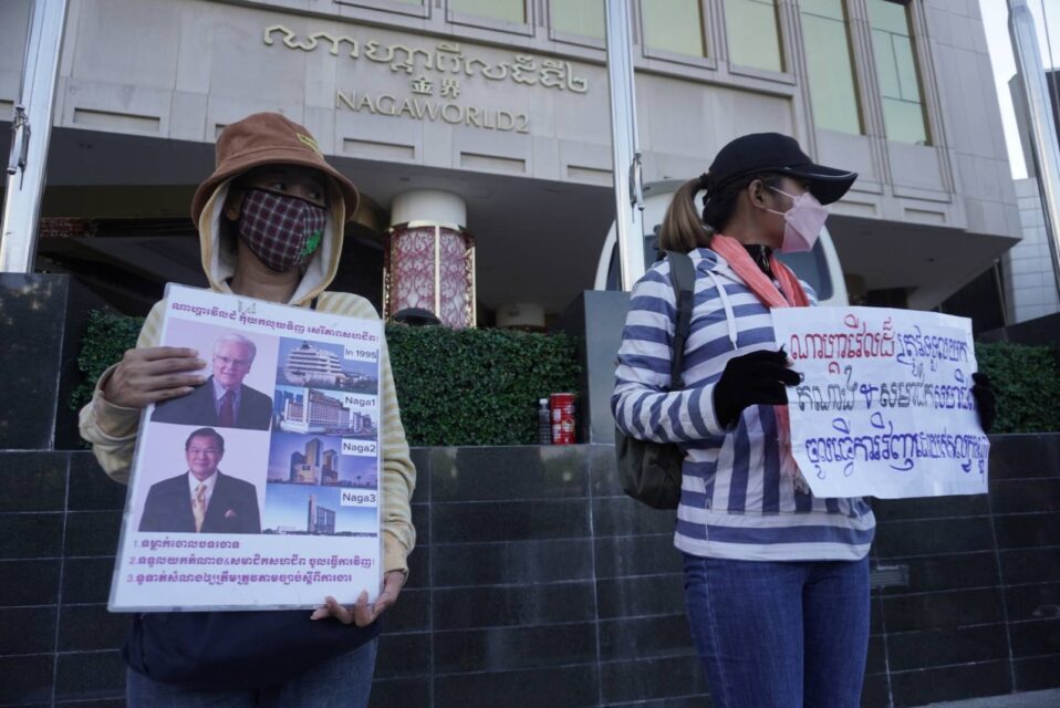Two NagaWorld strike participants hold signs in front of the Naga 2 building in Phnom Penh's Tonle Bassac district on November 9, 2022. (Kay Nara/VOD)