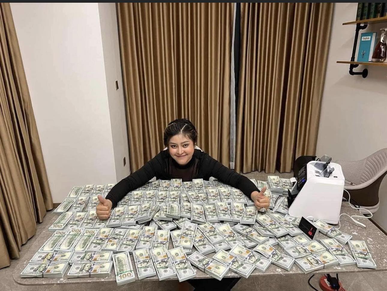 Oeun Molika holds two thumbs up over a table covered in stacks of hundred dollar bills, in a photo posted to the National Military Police Facebook page on December 14, 2022.