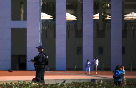 Tourists take photographs and walk near an Australian Federal policeman carrying a gun as he patrols the forecourt of Australia's Parliament House in Canberra, Australia, October 16, 2017. (David Gray/Reuters)