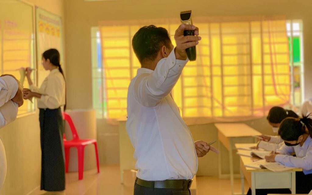 A teacher shows the students an electric razor. (Sampov Loun High School's Facebook)