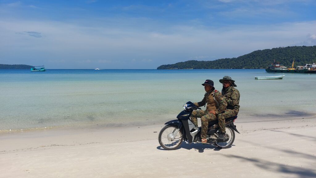 Two guards in camouflage drive a motorbike on the beach at Koh Rong Sanloem island's Saracen Bay resort area on February 4, 2023. (Danielle Keeton-Olsen/VOD)